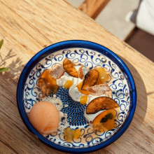 Eine blau-weiß gemusterte Schüssel mit Orangensorbet, Sahne, Fruchtsaucen und karamellisierten Scheiben auf einem Holztisch.